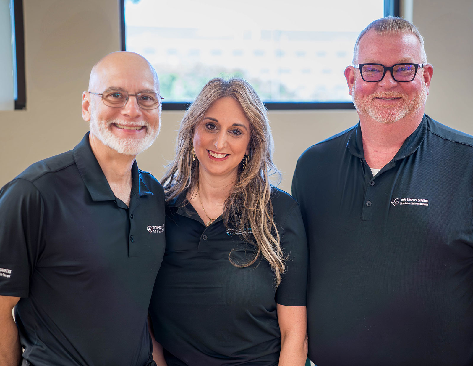 Three smiling people in matching black polo shirts.